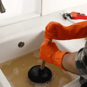 A plunger being used in a blocked sink full of dirty water
