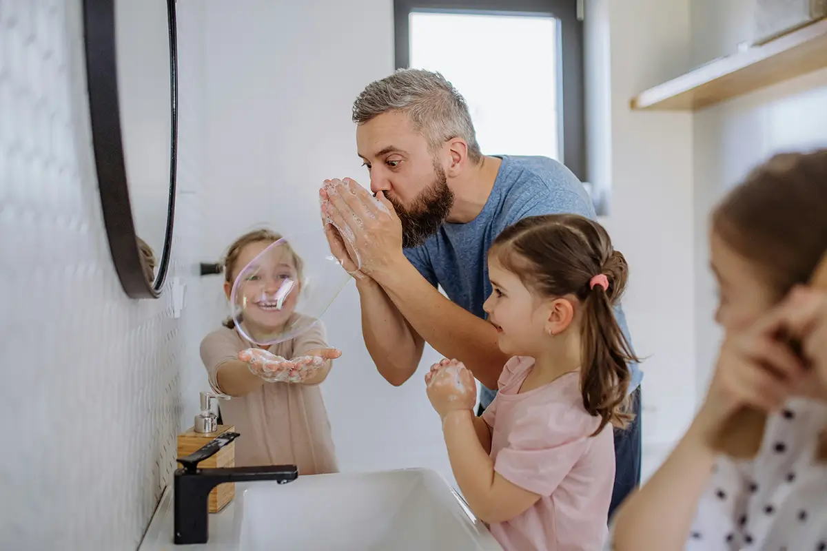 Father with children in the bathroom, blowing soapy bubbles at the sink